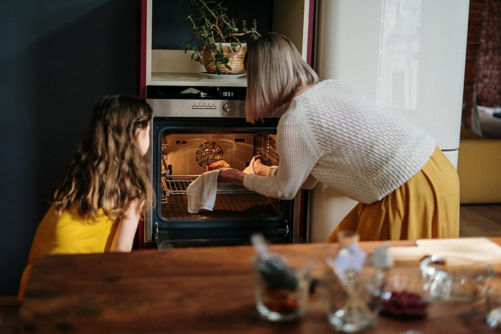 穿白织运动衫和黄裙子的女人 和女儿一起在炉子里做饭