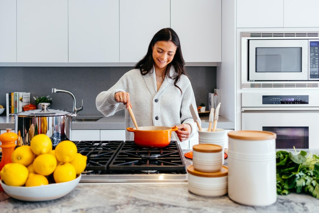 穿灰色毛衣的女人在厨房里做饭时 拿着木板和橙锅