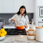 穿灰色毛衣的女人在厨房里做饭时 拿着木板和橙锅