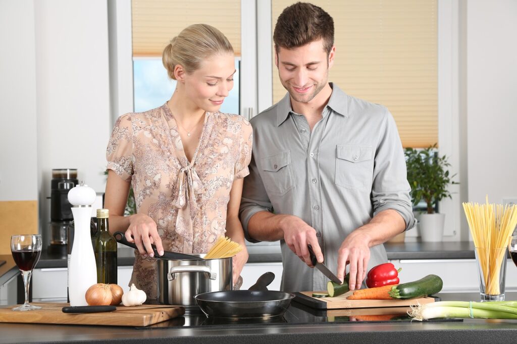 穿花纹礼服的女人站在一个穿灰色按钮的男子旁边,同时在厨房切片清菜