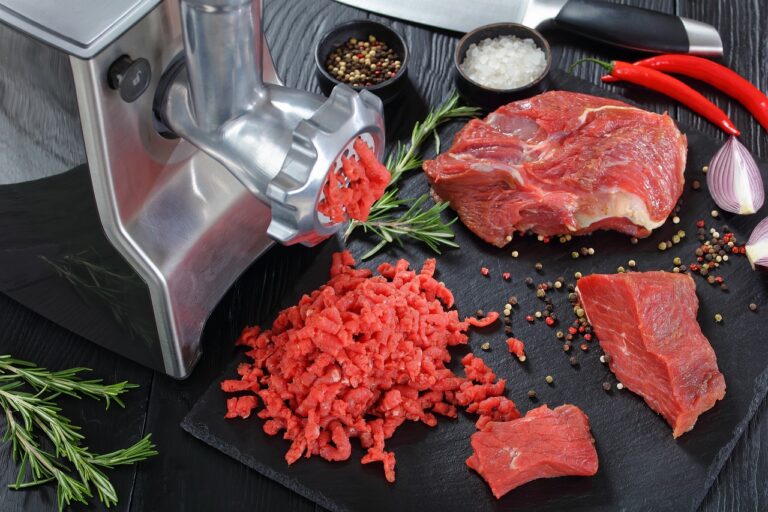 A silver meat grinder used to grind beef placed on a black chopping board