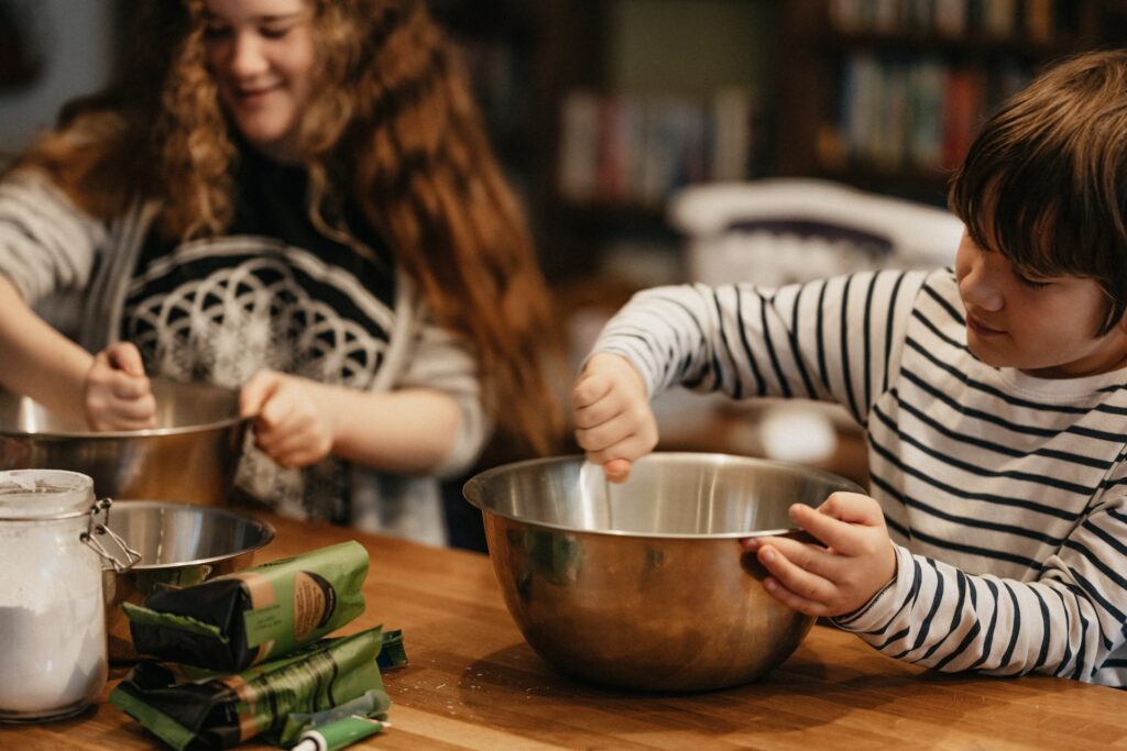 一位棕色卷发女人正在混合一个不锈碗 旁边的年轻男孩混合碗 在棕色木板上混合碗